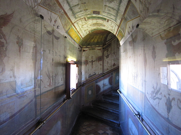 A hallway leading to some stairs. The walls are beautifully painted with pictures. 