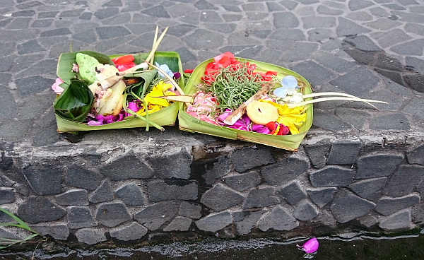 A couple of square leaf bowls with flower petals, food, and incense.