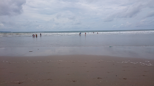 A beach with view outwards towards the ocean. Some people are in the distance, in the water.