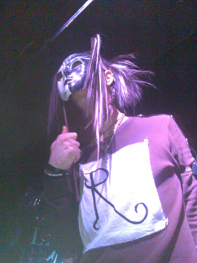 Lead singer of CrüxShadows holding a mask in front of his face.