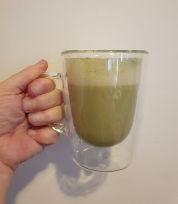 A hand holding a seethrough mug with matcha latte.