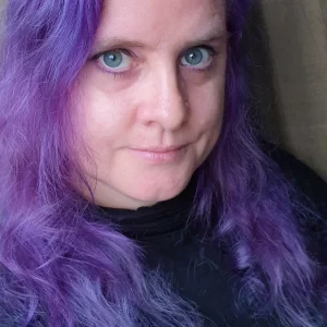 A photo of a woman with long, purple hair and black turtle neck sweater.