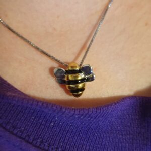A bee pendant on a silver necklace hanging around a throat.