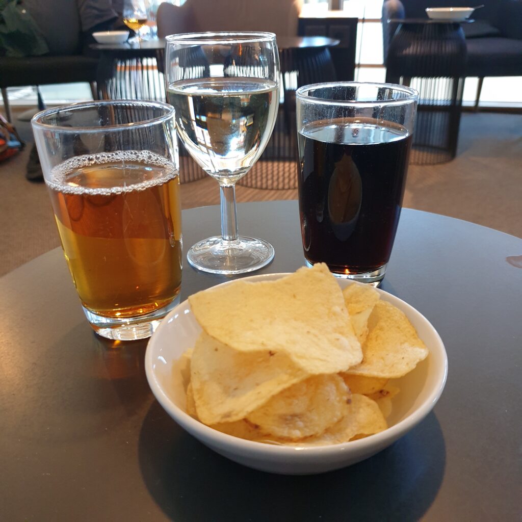 A table with a bowl of crisps, a glass of cola, a glass of apple juice, and a glass of white wine.