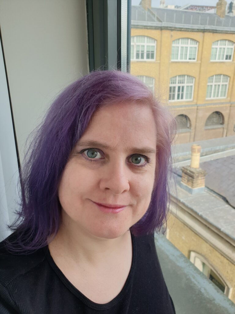 A woman with purple hair sitting in the window. In the background you can see brick buildings.