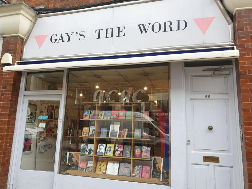 A bookshop front, you can see books in the window. The sign above it has pink triangles pointing down, one at each side of the text.