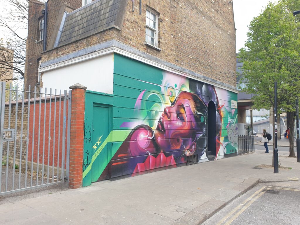 A building with on of its walls painted with a piece of street art. A black woman on a green brackround