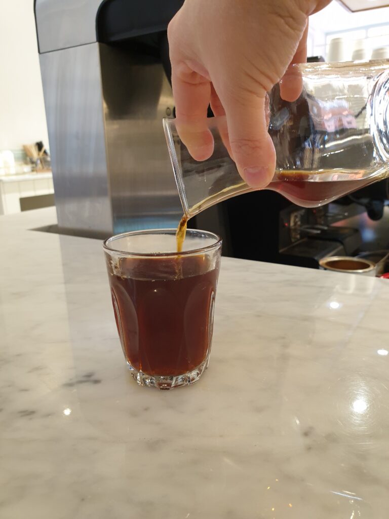 Ha hand holding a carafe of coffee, pouring it into a glass.