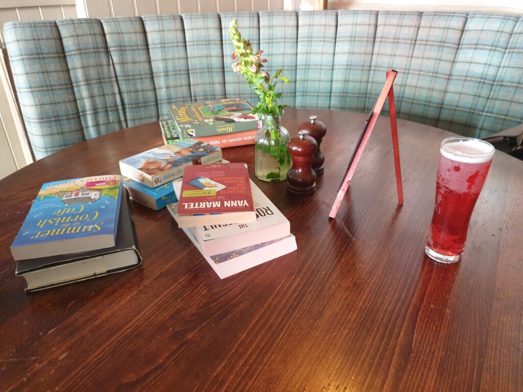 A table with books spread across it. On the table there's also a glass of red cider.