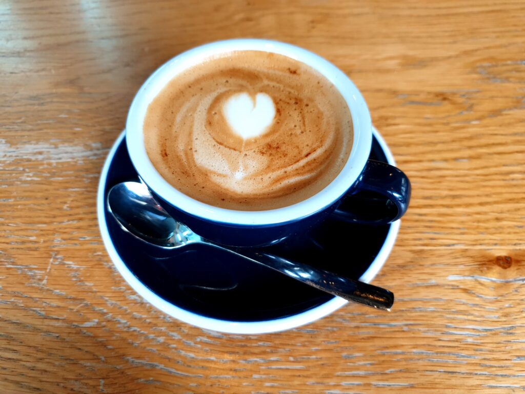 A cup of coffee with oat milk. A heart is formed in the oat milk as latte art.