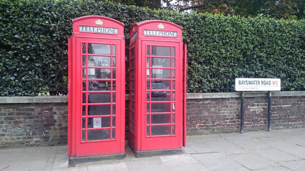 Two red phone booths in fron of a green hedge.