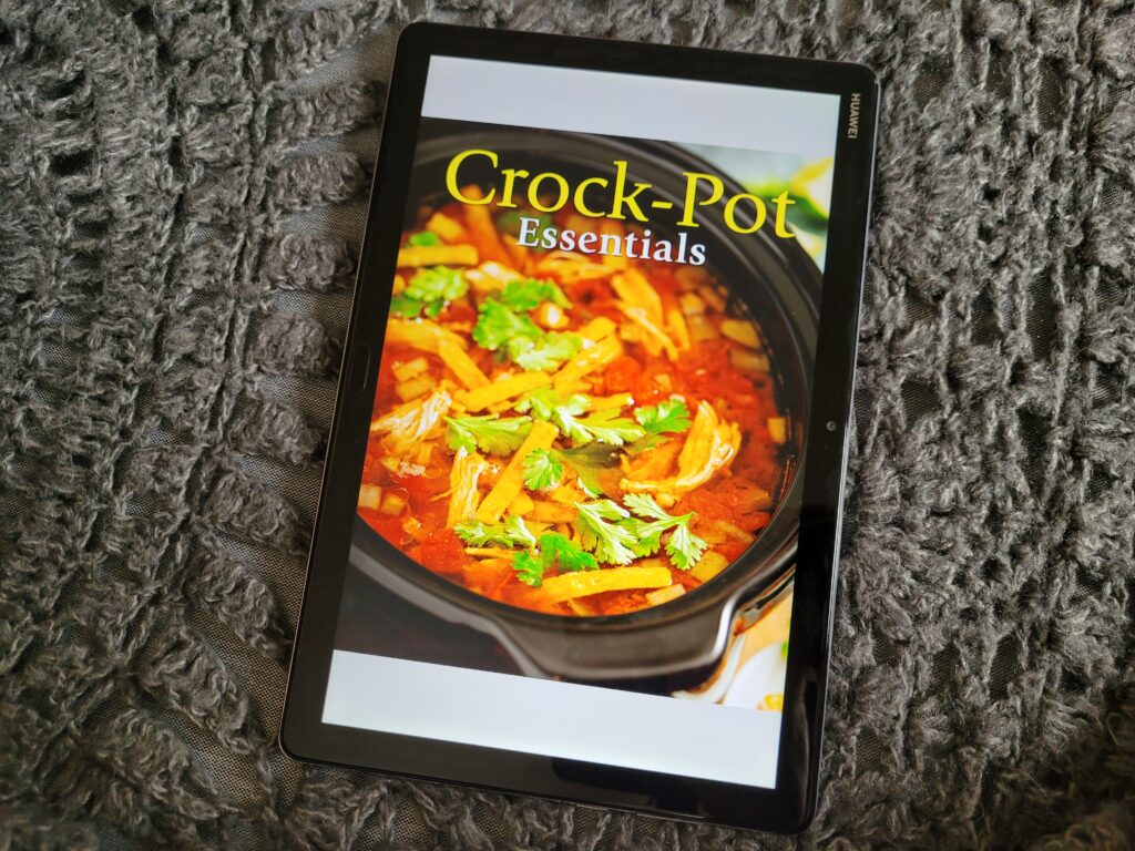 A tablet laying flat on top of a shawl, showing a tablet with the cover of the cookbook.